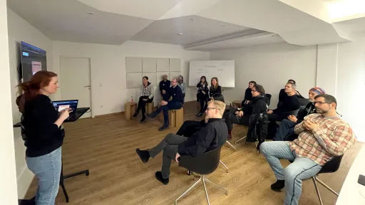 Marie hält eine Präsentation vor einer Gruppe aufmerksamer Menschen in einem Seminarraum.
